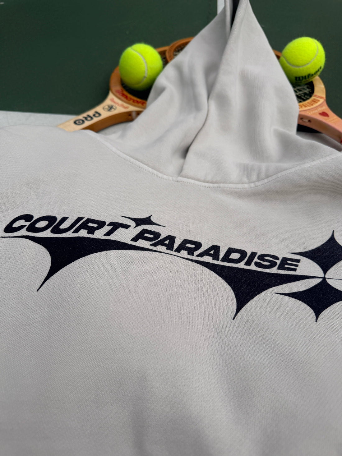 Court Paradise Bone hoodie on vintage wood tennis racquets with a tennis ball, foundational look for beginners