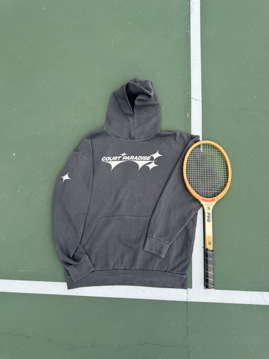 Double Trouble Hoodie in Charcoal on a green hard court, front chest wordmark, next to a wooden racquet